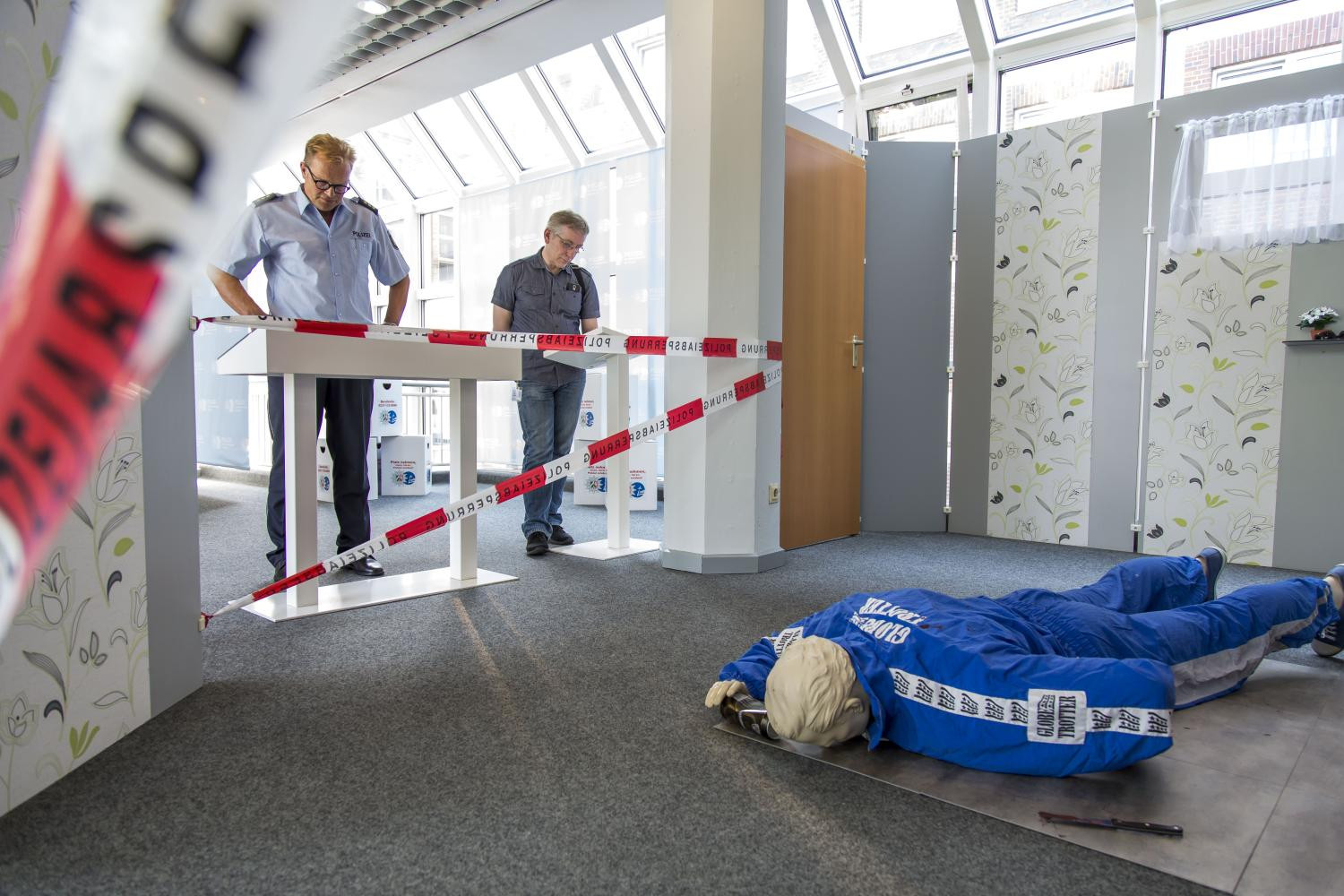 Zwei Männer stehen in einem Ausstellungsraum und betrachten je einen Schaukasten. Einer der Männer trägt eine Polizeiuniform.