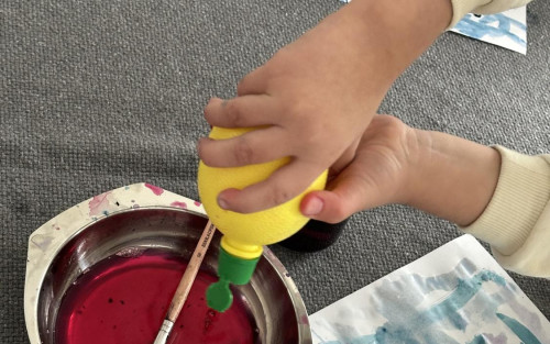 Das Bild zeigt Kinderhände, die Farben anmischen. Ein Kind hält Zitronensaft in der typischen Verpackung in den Händen und drück diesen in den Farbtopf.