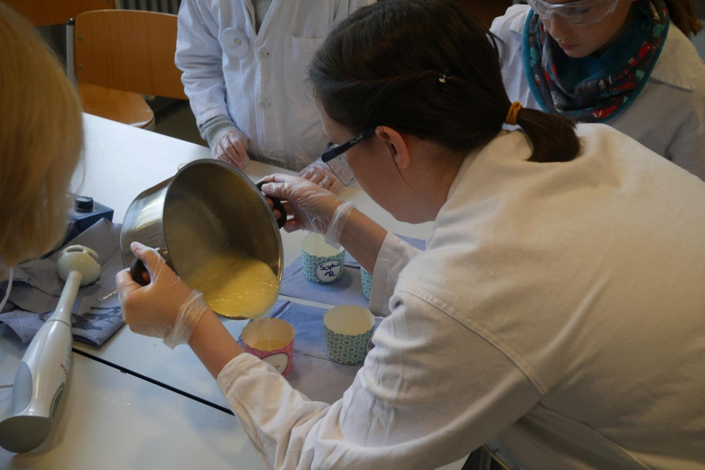 Menschen in Laborkitteln schütten Pudding in Tassen um.