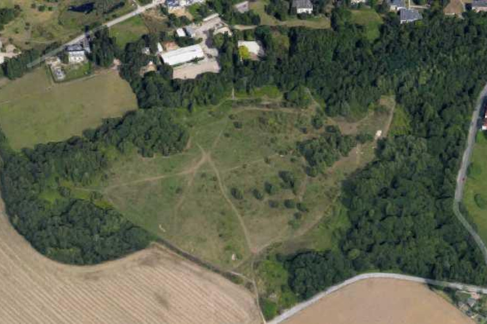 Ein Luftbild von einem Gelände, dass zwischen Feldern und Baumgruppen liegt. Die Fläche besteht aus Wiesen mit einigen Bäumen und Sträuchern. Am Rand des  Bildes stehen vereinzelt Häuser.