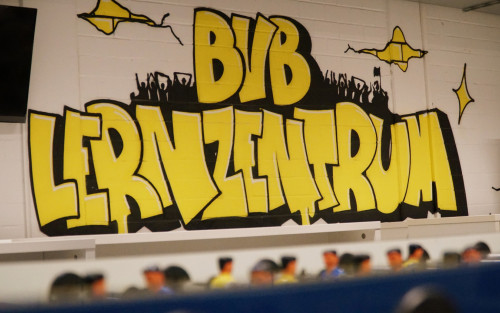 Auf einer weiß gestrichenen Ziegelwand ist ein schwarz-gelbes Graffiti aufgesprüht mit dem Schriftzug "BVB Lernzentrum".