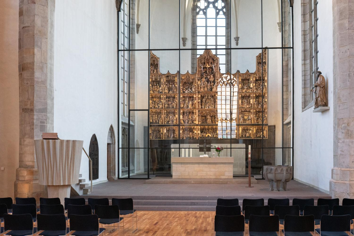 Der goldene Klappaltar mit biblischen Szenen im Altarraum der St. Petri Kirche. Der Altar befindet sich hinter einer Glaswand. Im Altarraum ist ein steinernen Taufbecken, davor einer steinerne Kanzel. Der gesamte Altarraum ist durch die hohen Fenster zu allen Seiten sehr hell.